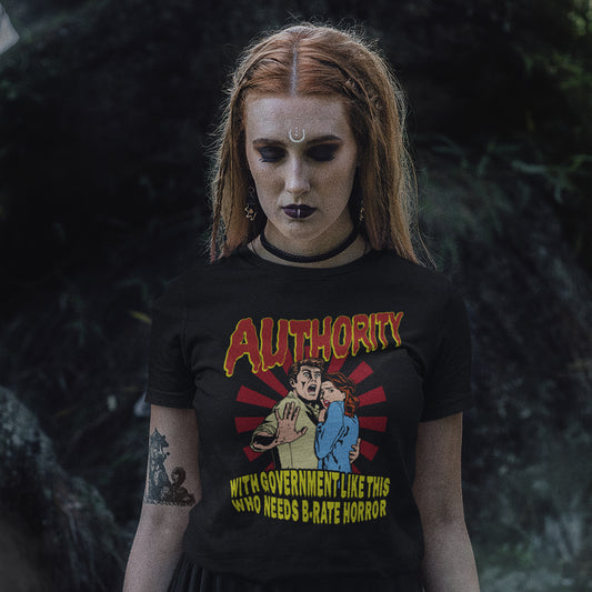Person wearing a black t-shirt with graphic design and text, standing against a dark background. This non conformist t shirt design is portrayed in an old horror movie poster. A witty but satirical view of just how bad our governance has become and how it resembles watching a B rate horror movie. Made from 100% organic ring-spun cotton, this anti government t shirt is unisex, high-quality, super comfy, and best of all, eco-friendly.