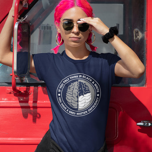 A woman with pink hair, standing against a van door, wearing sunglasses and a French navy blue short sleeved crew neck t-shirt with a graphic of a brain with the text" IF YOU ONLY THINK IN BLACK & WHITE, YOU HAVE A GREY MATTER DEFICIENCY" around it.