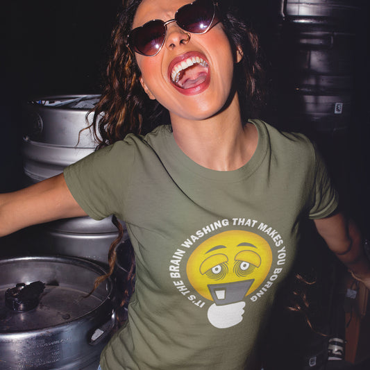A woman wearing sunglasses and sing, wearing a khaki t-shirt with "IT'S THE BRAIN WASHING THAT MAKES YOU BORING" written around an emoji on a smartphone.