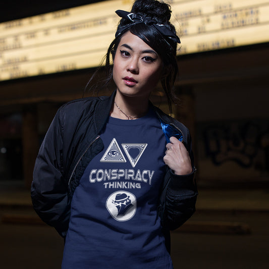 A woman wearing a French navy blue graphic t-shirt with a white graphic print on the front. The graphic features two triangles enclosing eyes and a heart, the words 'CONSPIRACY THINKING' in a distressed stencil font, and a circular logo of a man in a fedora and suit.