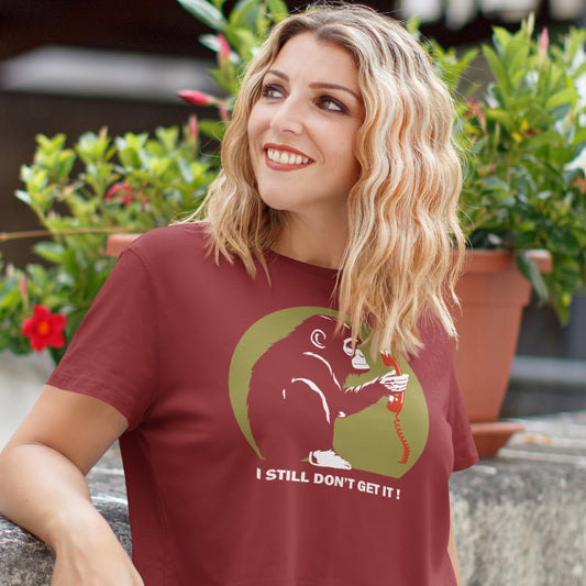Woman wearing a burgundy t-shirt with a graphic design and text, sitting outdoors with plants in the background. This anti smart phone abuse t-shirt design highlights the human obsession with smart phones and how strange it must look to an ape. An outsiders view of a world glued to mobile phones. Made from 100% organic ring-spun cotton, this anti mobile phone abuse t-shirt is unisex, high-quality, super comfy, and best of all, eco-friendly.