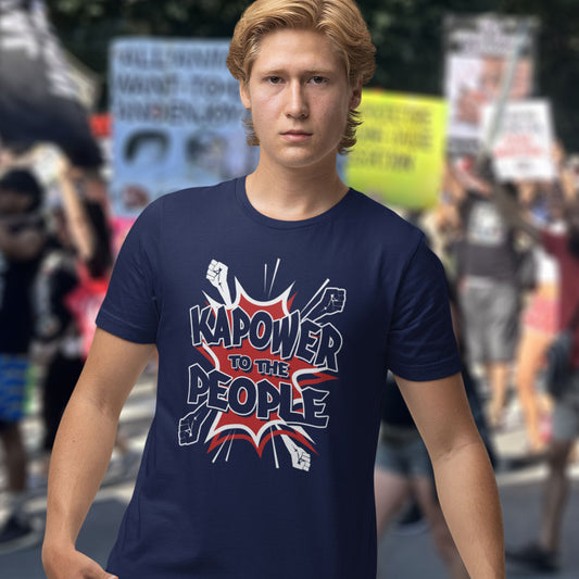 Person wearing a French navy blue t-shirt with 'Kapower to the People' text in a protest setting. This anti government t shirt packs a punch with this humorous play on the slogan 'Power to the people', with a comic book twist. Support true democracy with this funny political message. Made from 100% organic ring-spun cotton, this unisex non conformist t shirt is a total must-have. It's high-quality, super comfy, and best of all, eco-friendly.