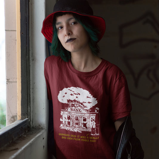 Woman with green hair standing in a window, wearing a burgundy t-shirt with a design of a run down Bank.