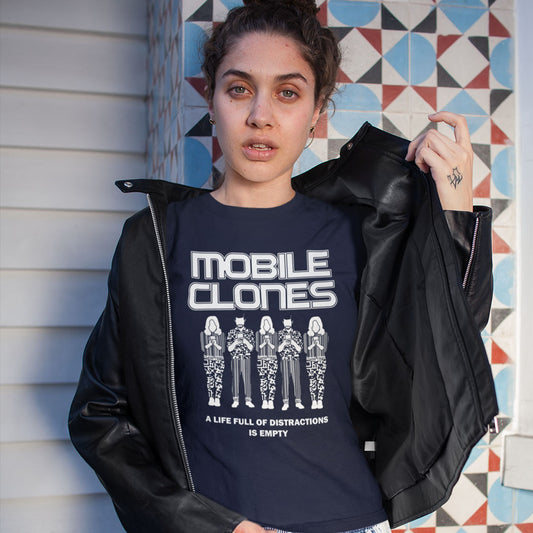 A woman holding her jacket open to show a French navy t-shirt featuring a white graphic print on the front. The graphic displays the text 'MOBILE CLONES' above five stylized figures, with the phrase 'A LIFE FULL OF DISTRACTIONS IS EMPTY' below.