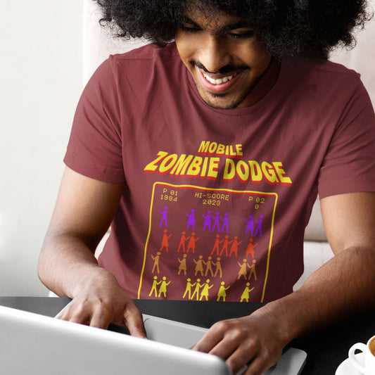 Person wearing a t-shirt with 'Mobile Zombie Dodge' design, using a laptop. A satirical gamer t-shirt design for anyone who feels they are in a repetitive 80's video game every time they enter a crowded street scene. Welcome to the age of the mobile phone and lack of social awareness. Made from 100% organic ring-spun cotton, this unisex gamer t-shirt is alternative and original. It's high-quality, super comfy, and best of all—eco-friendly.