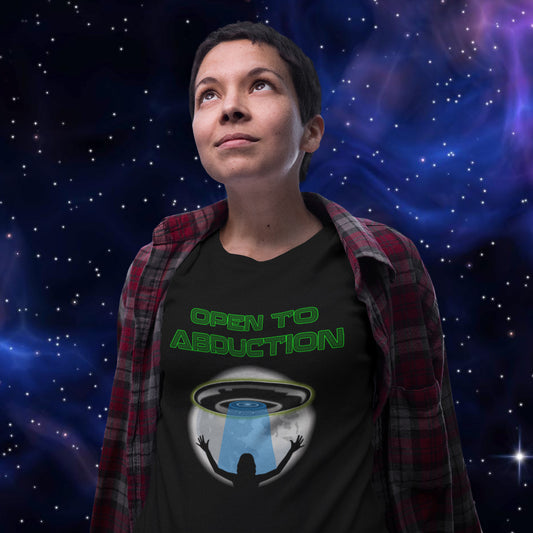 A woman wearing a black graphic t-shirt with green text reading 'OPEN TO ABODUCTION' and a UFO/space graphic, styled with an open red plaid flannel shirt over her shoulders, set against a starry outer space background.