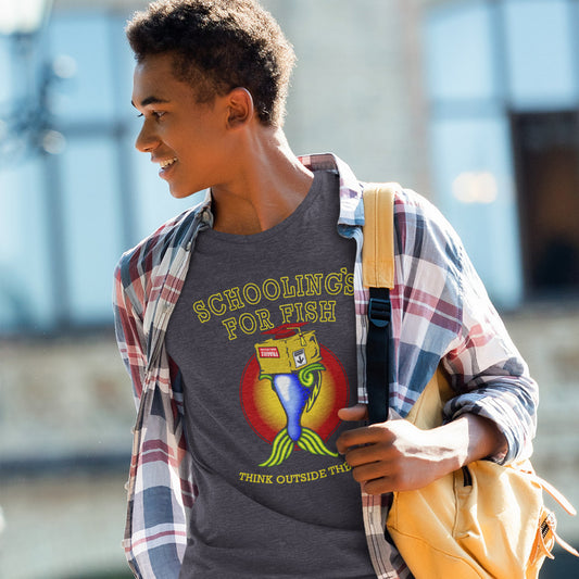 A young man wearing a dark gray graphic t-shirt with a colorful fish illustration and the text 'SCHOOLING FOR FISH' and 'THINK OUTSIDE THE BOX'. He has on an open plaid flannel shirt and a yellow backpack, set against a blurred outdoor background.