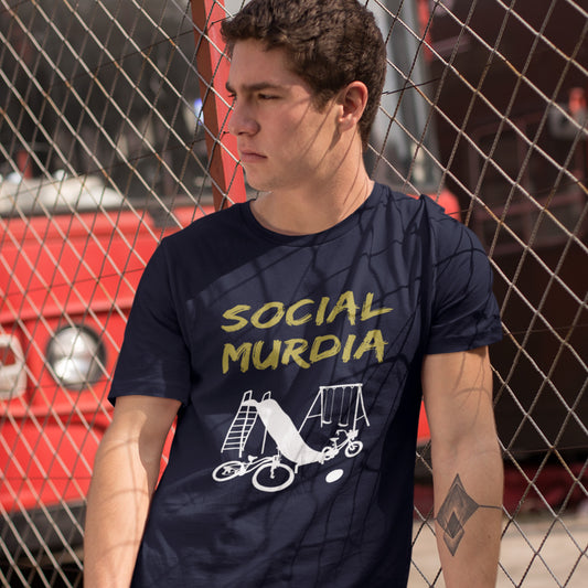 Person wearing a French navy blue t-shirt with 'SOCIAL MURDIA' text and graphic design, standing in front of a red vehicle. This counterculture t-shirt promoting social awareness of the effect of social media on our children. A unique design depicting how social media is probably murdering our society and leaving our playgrounds empty. Made from 100% organic ring-spun cotton, this anti-mobile phone t-shirt is unisex, high-quality, super comfy, and best of all, eco-friendly.