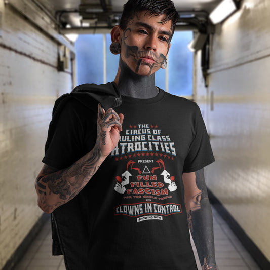 A heavily tattooed man standing in a public corridor with his jacket over his shoulder, wearing a black short sleeved crew neck t-shirt with a spoof circus poster design named "The Circus of Ruling Class Atrocities" and "Clowns in Control" text.