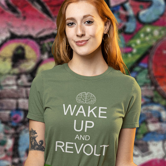A woman with red hair wearing an khaki green t-shirt t-shirt short-sleeve crewneck t-shirt with a white graphic print on the front. The print features a simple line-art brain icon above the text 'WAKE UP AND REVOLT' in a bold, sans-serif font, styled like the classic 'Keep Calm' poster.