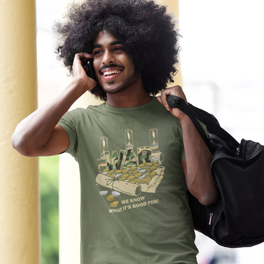 A man with a large black afro is smiling and talking on a phone while wearing an olive green graphic t-shirt. The shirt features a graphic of a map filled with gold coins and bottles, with the word 'WAR'.