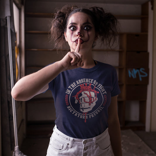 Person wearing a blue t-shirt with graphic design, making a shushing gesture in an indoor setting. This social issues t shirt plays on the saying 'In the absence of light, darkness prevails' with a political message encouraging people to put their apathy and denial aside and fight for their rights before they are taken advantage of. Made from 100% organic ring-spun cotton, this human rights t shirt is unisex, high-quality, super comfy, and best of all, eco-friendly.