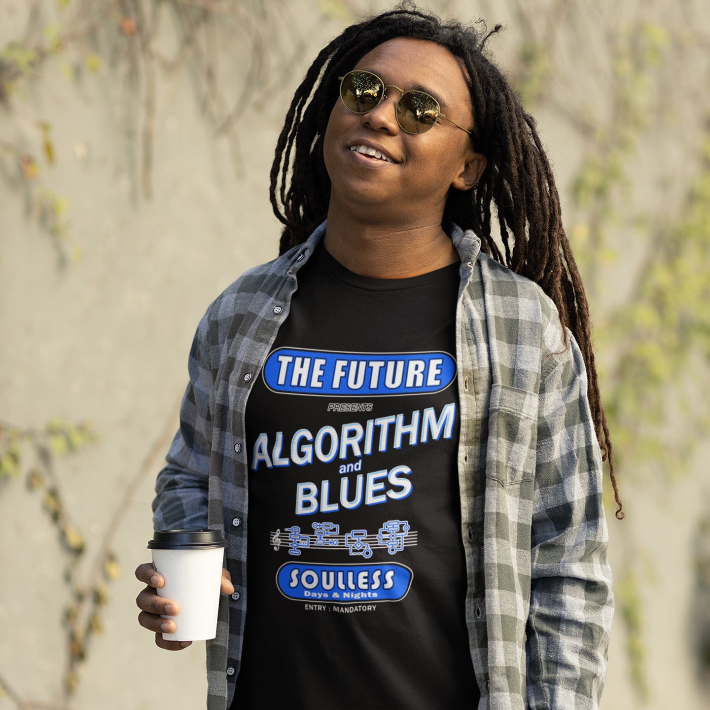 Person wearing a black t-shirt with text and graphics, holding a coffee cup outdoors. This sign of the times t shirt design is a play on an old music poster and an alternative view of what the future may hold in a world that is decided on algorithms. Made from 100% organic ring-spun cotton, this social awareness t shirt is unisex, high-quality, super comfy, and best of all, eco-friendly.