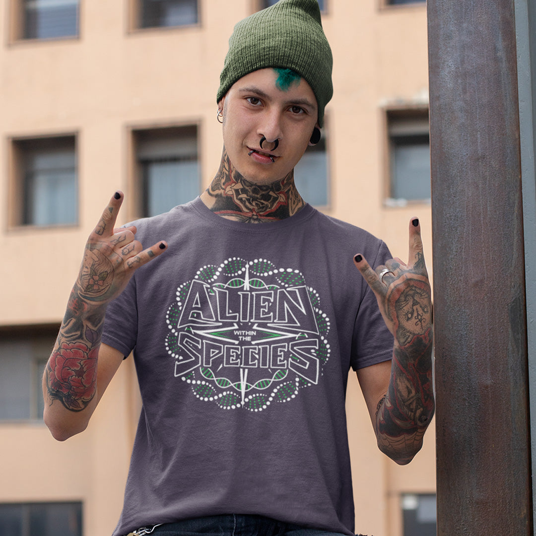 Person wearing a 'Alien Within Species' t-shirt with tattoos and a green beanie, standing against a building. This non conformist t shirt expands the use of the word 'Alien'. This design is ideal for everyone that feels they don't truly relate to the rest of humankind and modern society. Made from 100% organic ring-spun cotton, this counter culture t-shirt is unisex, high-quality, super comfy, and best of all, eco-friendly.