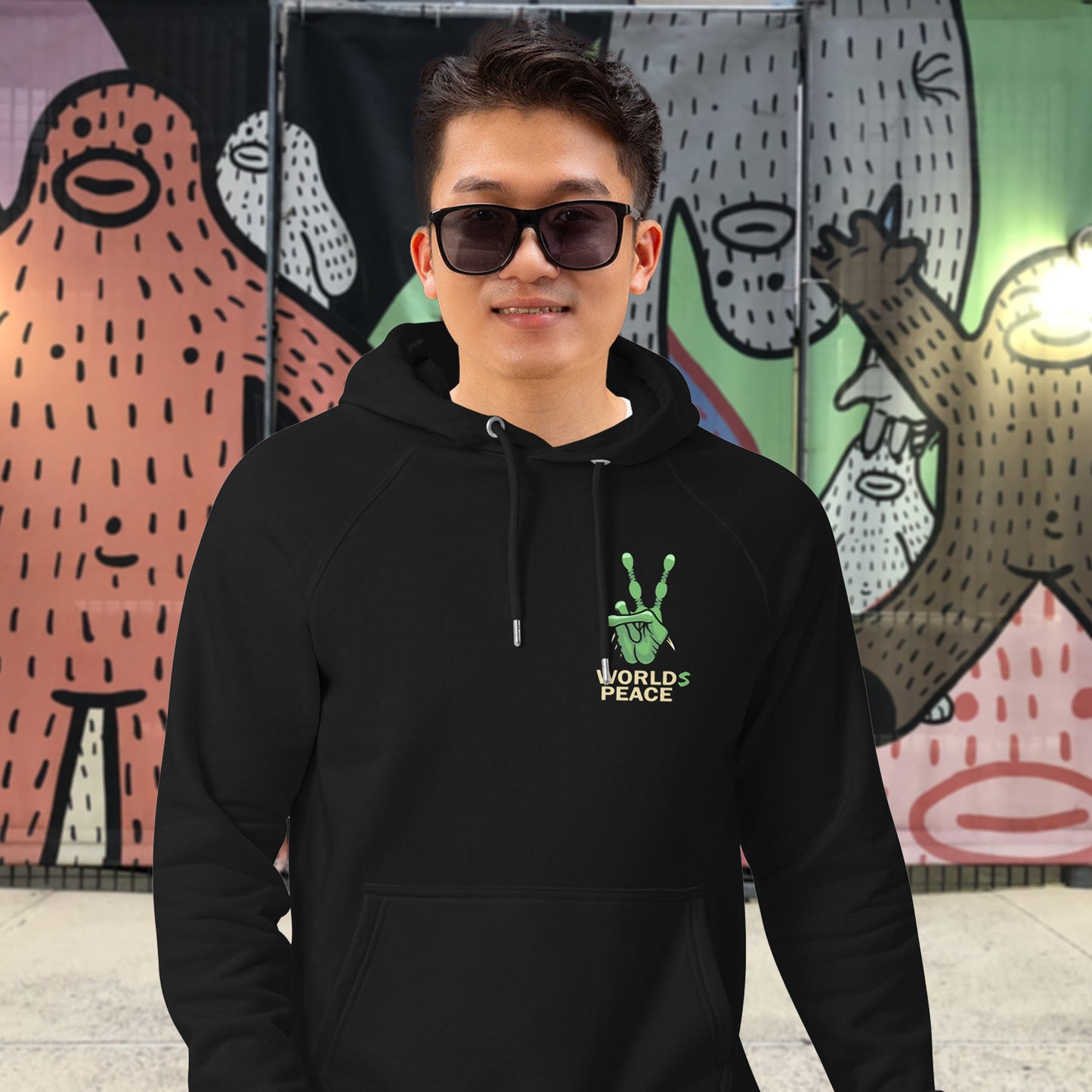 Person wearing a black hoodie with a peace symbol design in front of a colourful mural. A world peace hoodie with an alien lovers twist. When we think of world peace lets not be selfish about it., lets include all Worlds. Comfortable and practical. It's extra soft and has a convenient front pouch pocket. Made from organic cotton and recycled polyester, this unique alien hoodie is the perfect eco-friendly choice.