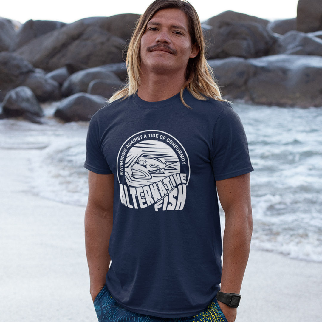 Man standing on a beach wearing a French navy blue t shirt with An "ALTERNATIVE FISH" logo.