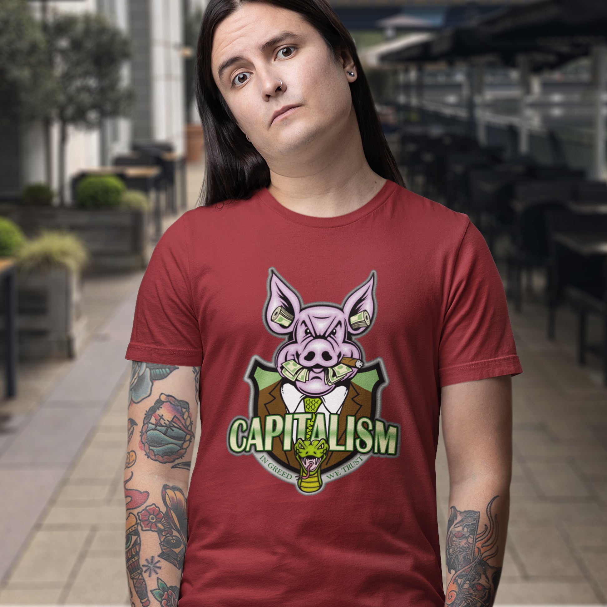 Person wearing a red t-shirt with a pig graphic and 'CAPITALISM' text in an urban setting
