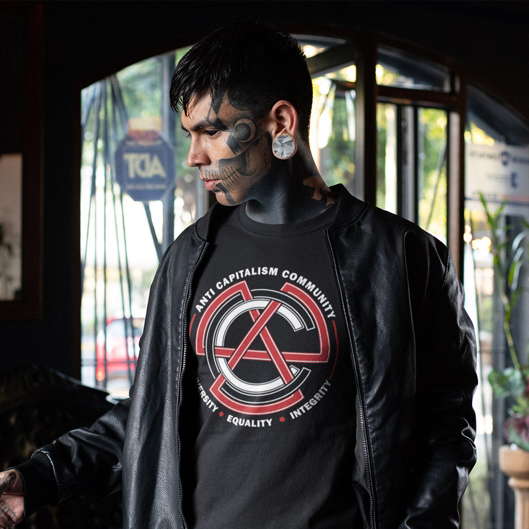 Person wearing a black t-shirt with a red and white logo and text, standing indoors. This anti establishment t shirt speaks out against capitalism and promotes diversity, equality and integrity. Capitalism is responsible for so many of societies problems, do not accept it. Join our community and be proud to wear the shirt. Made from 100% organic ring-spun cotton, this anti capitalist t shirt is unisex, high-quality, super comfy, and best of all, eco-friendly.