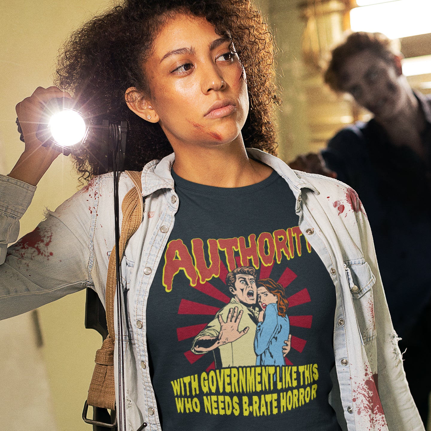 Person wearing a t-shirt with graphic design and text, standing in a room with another person in the background. This non conformist t shirt design is portrayed in an old horror movie poster. A witty but satirical view of just how bad our governance has become and how it resembles watching a B rate horror movie. Made from 100% organic ring-spun cotton, this anti government t shirt is unisex, high-quality, super comfy, and best of all, eco-friendly.