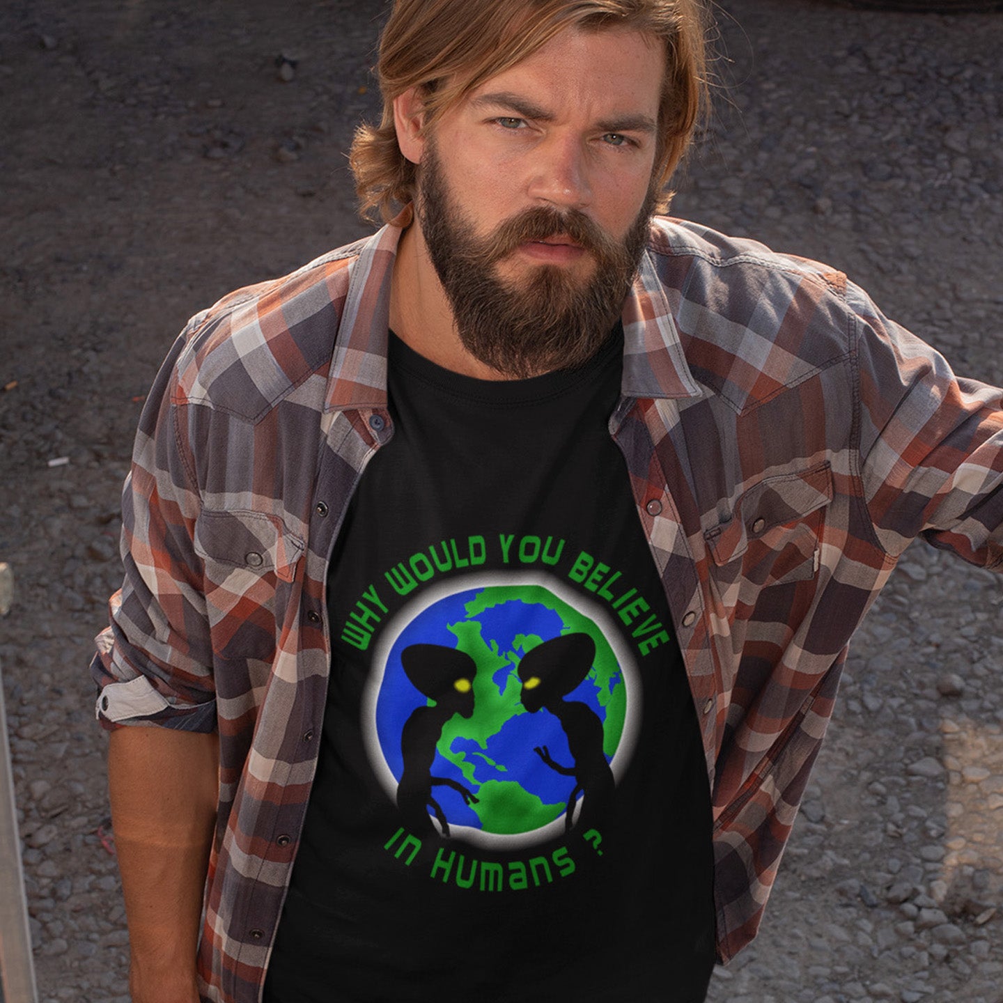 Man wearing a black t-shirt with a graphic design and plaid shirt over it, standing against a dark background. A funny conspiracy theory t shirt with a play on words design. We question whether or not to believe in aliens but with so much evidence around is it not a more important question to wonder if they have lost their faith in us. Made from 100% organic ring-spun cotton, this conspiracy theorist t shirt is unisex, high-quality, super comfy, and best of all, eco-friendly.