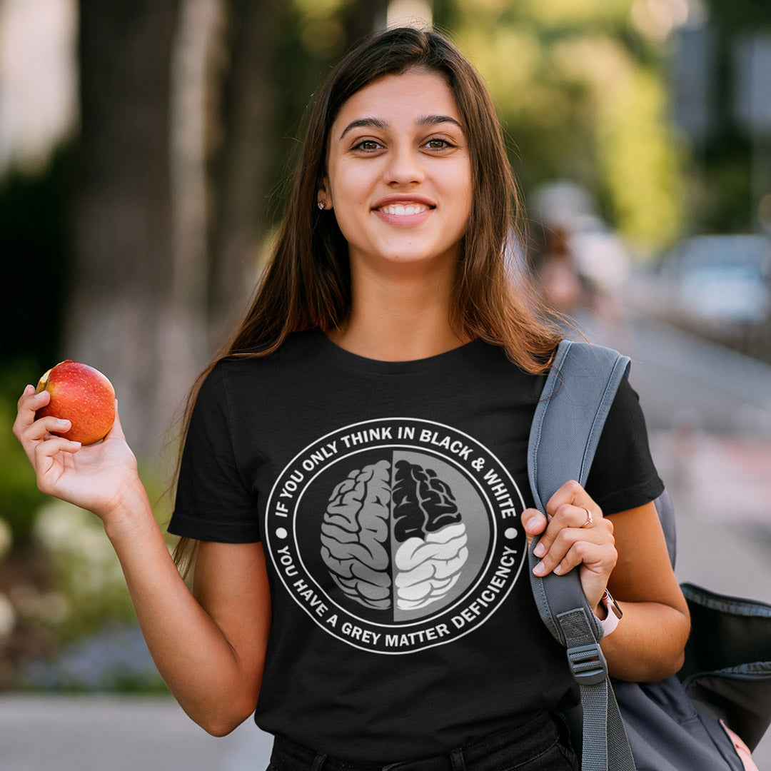 Woman wearing a black t-shirt with a graphic design, holding an apple outdoors. A stencil art t shirt design. It would be so easy if life was black and white, but it's the grey area where all the thinking and personal growth is done. A philosophy t shirt design for people who see the detail and can think outside the box. Made from 100% organic ring-spun cotton, this social awareness t shirt is unisex, high-quality, super comfy, and best of all, eco-friendly.