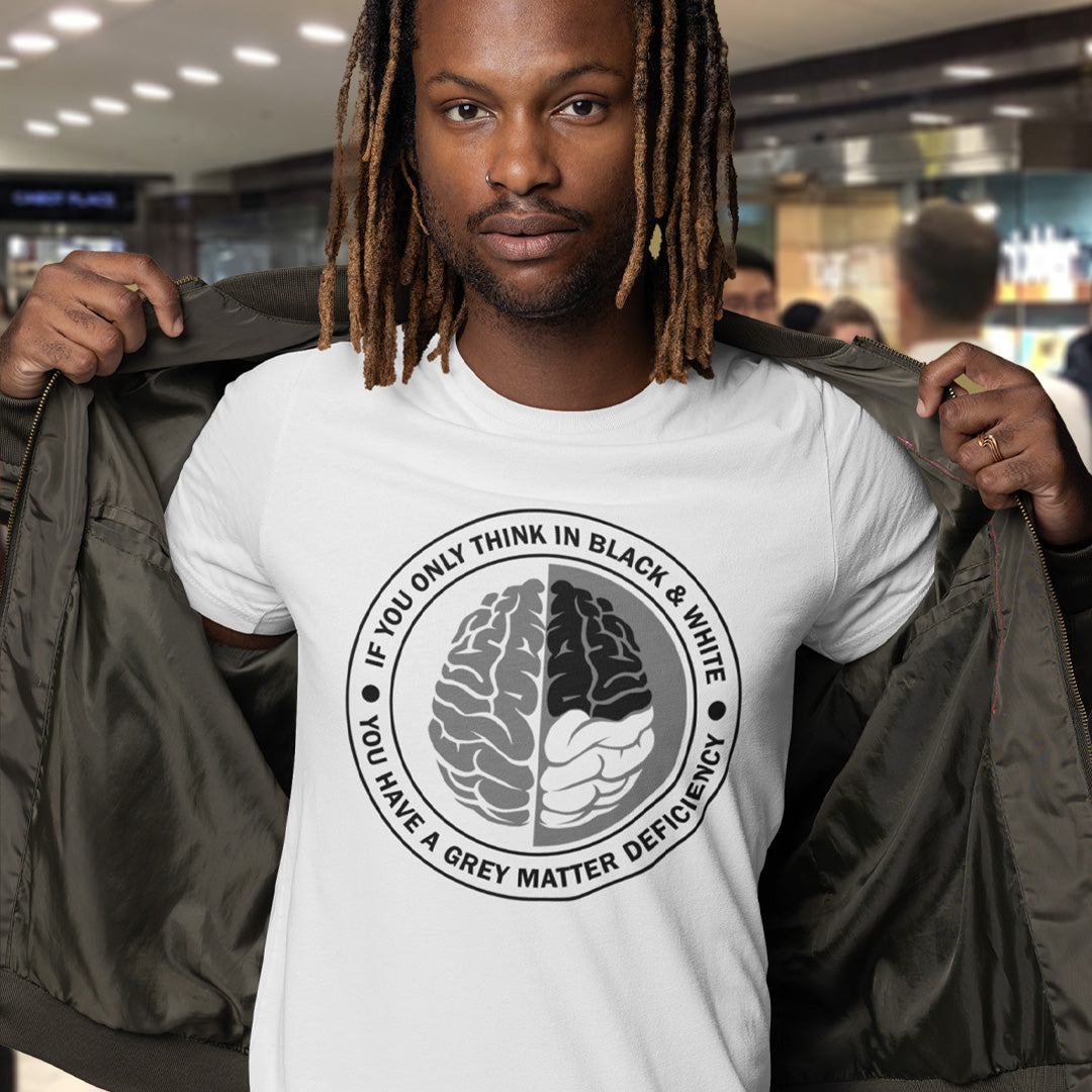 A man with dreadlocks, holding his jacket open to reveal a white short sleeved crew neck t-shirt with a graphic of a brain with the text" IF YOU ONLY THINK IN BLACK & WHITE, YOU HAVE A GREY MATTER DEFICIENCY" around it. 