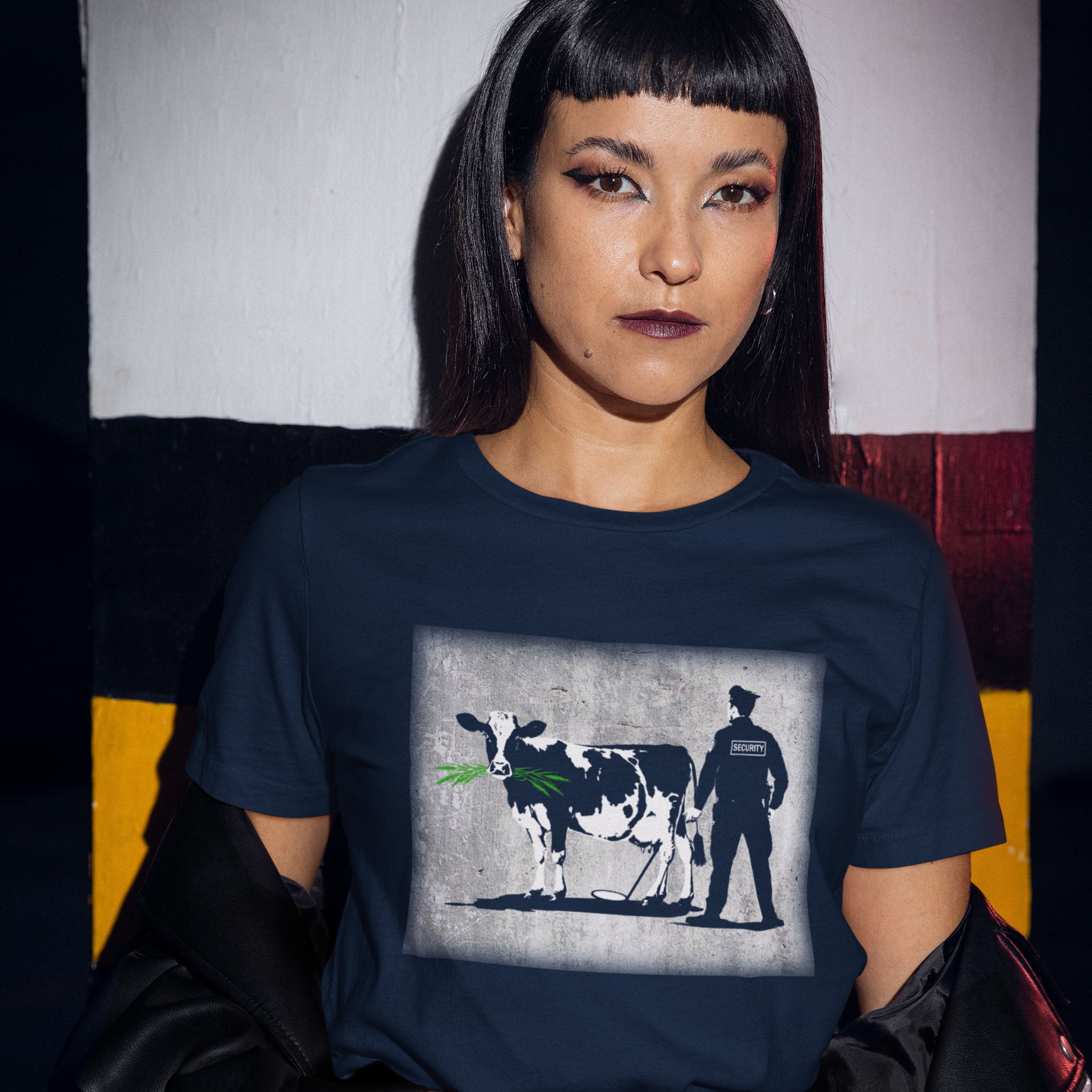 Person wearing a navy blue t-shirt with a graphic design of a cow and a person on a chair. A graffiti stencil art t-shirt showing the thin line between security and invasion of privacy highlighted with a touch of satire and sarcasm. Made from 100% organic ring-spun cotton, this Banksy style stencil graffiti t-shirt is unisex, high-quality, super comfy, and best of all, eco-friendly.