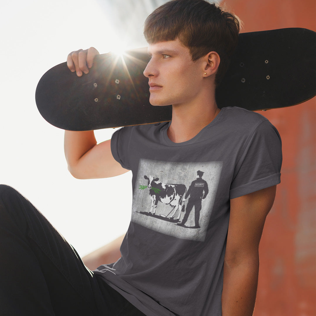 Person wearing an anthracite grey t-shirt with a graphic design of a cow and a person, holding a skateboard. A stencil graffiti t shirt showing the thin line between security and invasion of privacy, highlighted with a touch of satire and sarcasm. Made from 100% organic ring-spun cotton, this urban art t shirt is unisex, high-quality, super comfy, and best of all, eco-friendly.