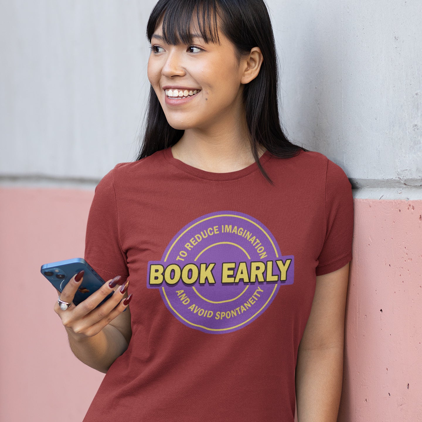 Person wearing a burgundy t-shirt with a purple and yellow graphic and text, holding a phone. A satirical and sarcastic t-shirt design highlighting the lack of spontaneity and imagination in modern life. The more efficient we make society the more we kill the essence and wonder of life. Made from 100% organic ring-spun cotton, this satirical and sarcastic t-shirt is unisex, high-quality, super comfy, and best of all, eco-friendly.