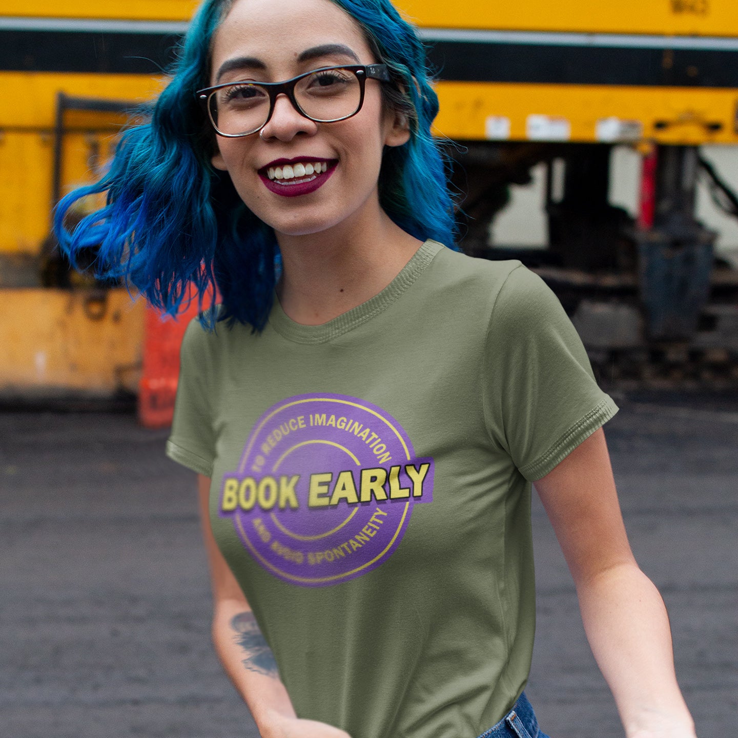Girl with blue hair wearing a 'Book Early' t-shirt outdoors. A satirical and sarcastic t-shirt design highlighting the lack of spontaneity and imagination in modern life. The more efficient we make society the more we kill the essence and wonder of life. Made from 100% organic ring-spun cotton, this satirical and sarcastic t-shirt is unisex, high-quality, super comfy, and best of all, eco-friendly.