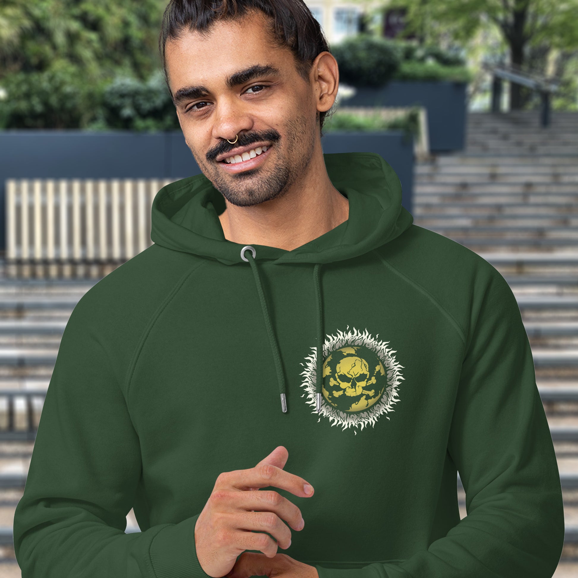 Man wearing a bottle green hoodie with a logo on it, standing outdoors. This environmental hoodie is concerned with global warming. A design to keep climate issues at the forefront of peoples minds. A burning issue. Made from 100% organic ring-spun cotton, this environmental awareness hoodie is unisex, high-quality, super comfy, and best of all, eco-friendly.