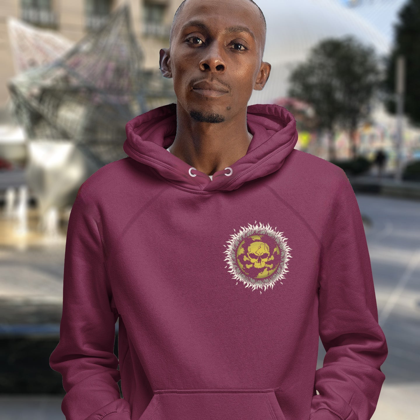 Man wearing a burgundy hoodie with a colourful emblem in an urban setting. This environmental hoodie is concerned with global warming. A design to keep climate issues at the forefront of peoples minds. A burning issue. Made from 100% organic ring-spun cotton, this environmental awareness hoodie is unisex, high-quality, super comfy, and best of all, eco-friendly.