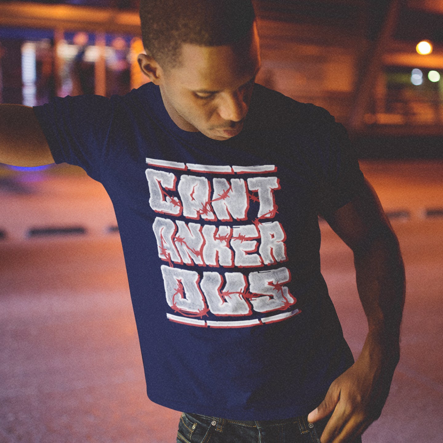 Man wearing a French navy blue t-shirt with red and white text, standing in an urban setting at night. A grumpy non conformist t shirt design. Argumentative and pessimistic ? Exercise your disapproval, and be proud to be labelled cantankerous. Made from 100% organic ring-spun cotton, this urban art t shirt is unisex, high-quality, super comfy, and best of all, eco-friendly.