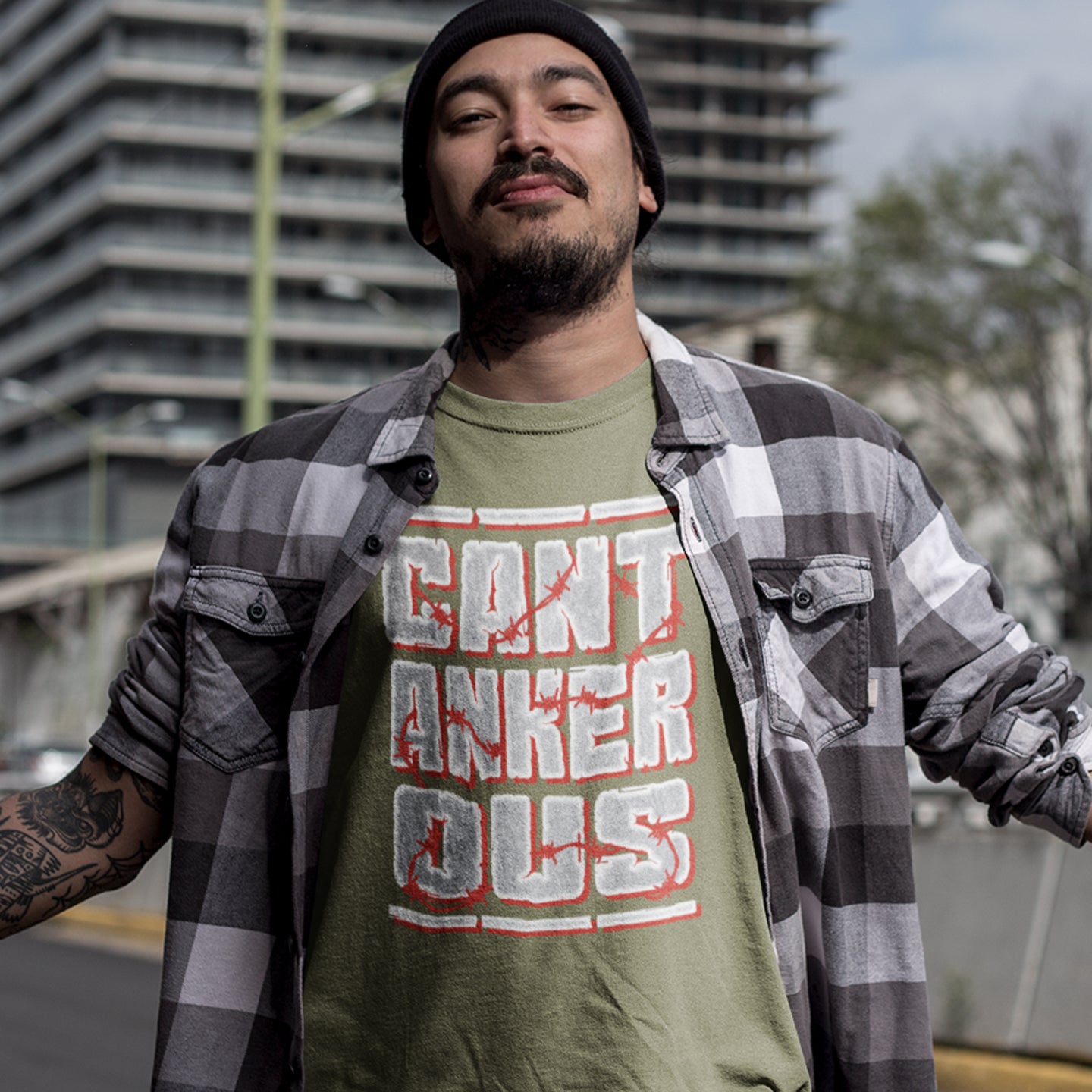 Man wearing a khaki t-shirt with text and a plaid shirt outdoors. A grumpy non conformist t shirt design. Argumentative and pessimistic ? Exercise your disapproval, and be proud to be labelled cantankerous. Made from 100% organic ring-spun cotton, this urban art t shirt is unisex, high-quality, super comfy, and best of all, eco-friendly.