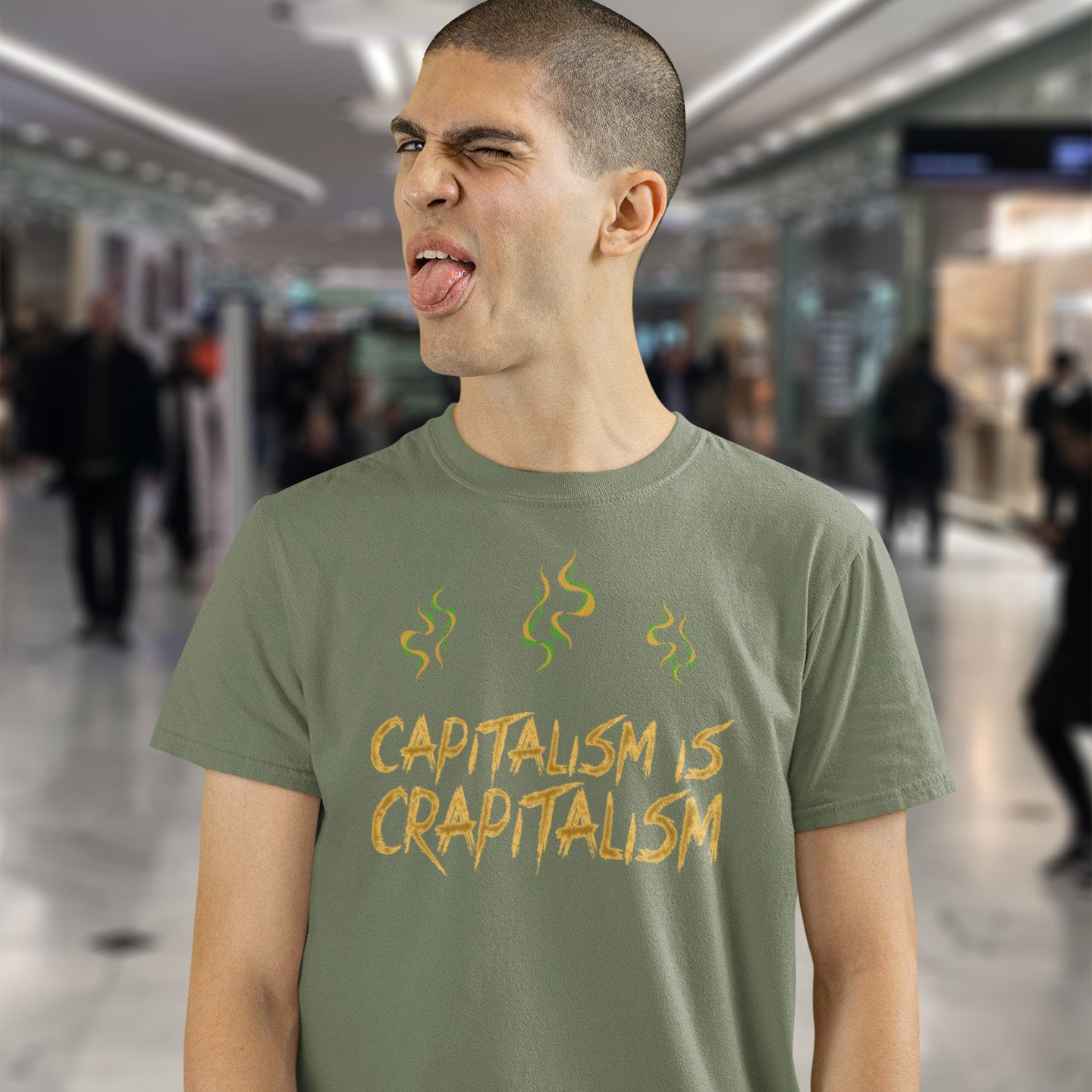 Person wearing a khaki t-shirt with 'CAPITALISM IS CRAPITALISM' text in a blurred indoor setting. A funny anti-capitalism t-shirt suggesting a letter was left out of the naming of capitalism. This unique anti-establishment t-shirt design argues that the system is crap. Made from 100% organic ring-spun cotton, this anti-capitalist t-shirt is unisex, high-quality, super comfy, and best of all, eco-friendly.