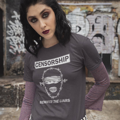 Person wearing a t-shirt with 'Censorship Benefits the Liars' design in front of graffiti. This civil rights t shirt highlights the negative benefits of censorship. Lies and censorship go hand-in-hand as tools of control and manipulation. This unique design promotes social awareness and freedom of speech. Made from 100% organic ring-spun cotton, this no censorship t shirt is unisex, high-quality, super comfy, and best of all, eco-friendly.