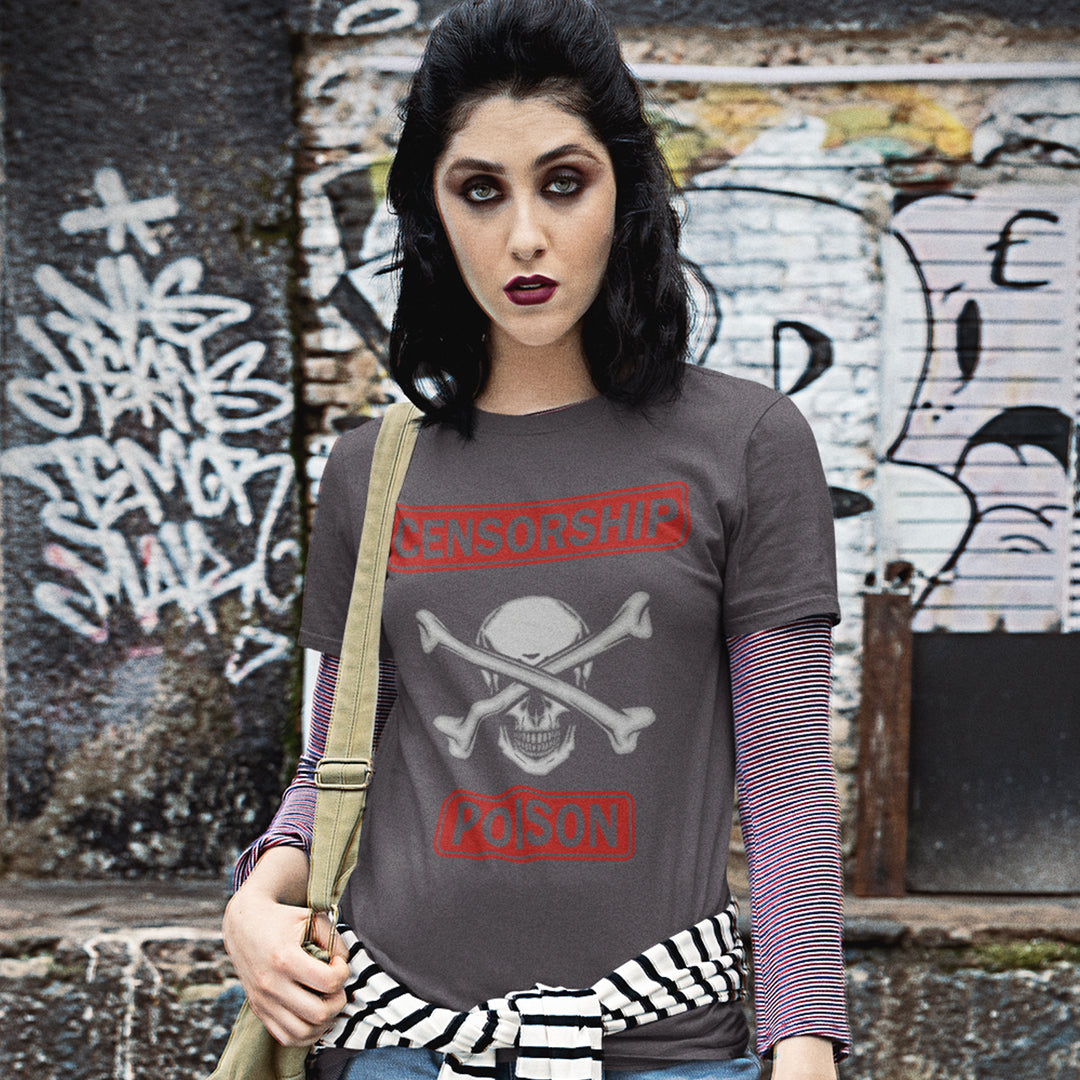 A woman wearing a dark gray graphic t-shirt with a skull and crossbones design and red text, layered over a purple striped long-sleeve shirt, standing in front of a graffiti-covered wall.