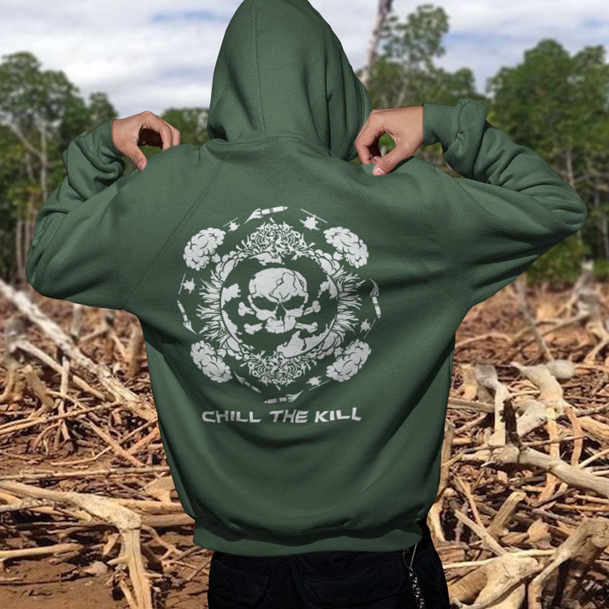 Green hoodie with skull design and 'Chill the Kill' text, worn outdoors. A 'save the planet' hoodie about human impact on nature. An Earth day special. This design highlights the amount of death and destruction we create as a species. Comfortable and practical. It's extra soft and has a convenient front pouch pocket. Made from organic cotton and recycled polyester, this anti-war political hoodie is a great eco-friendly choice.