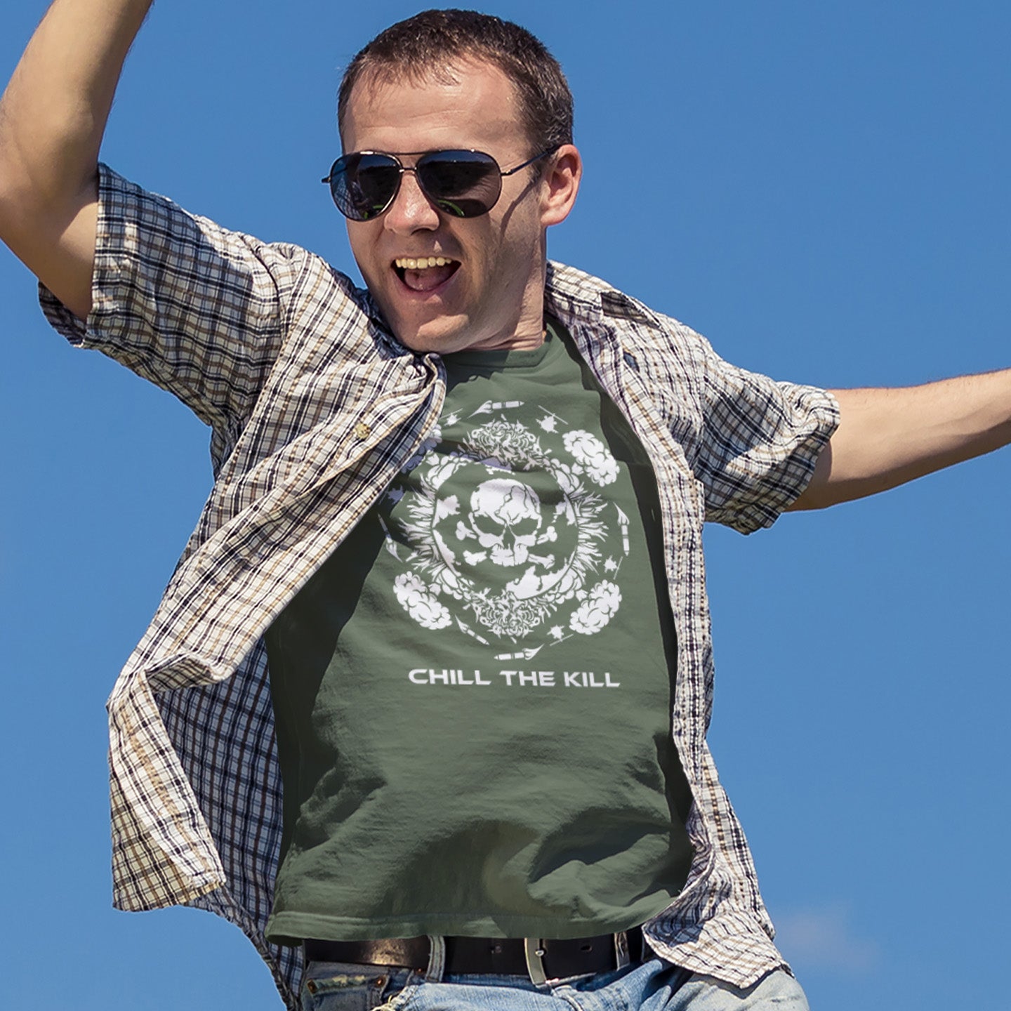 Man wearing a khaki t-shirt with 'Chill the Kill' design and sunglasses against a clear blue sky. An original save the planet t-shirt. A unique creation in a series of designs about environmental issues and climate concern. This one highlighting the amount of death and destruction we create as a species. Express your counterculture alternative view and encourage social awareness. Made from 100% organic ring-spun cotton, this political t-shirt is unisex, high-quality, super comfy, and best of all, eco-friend