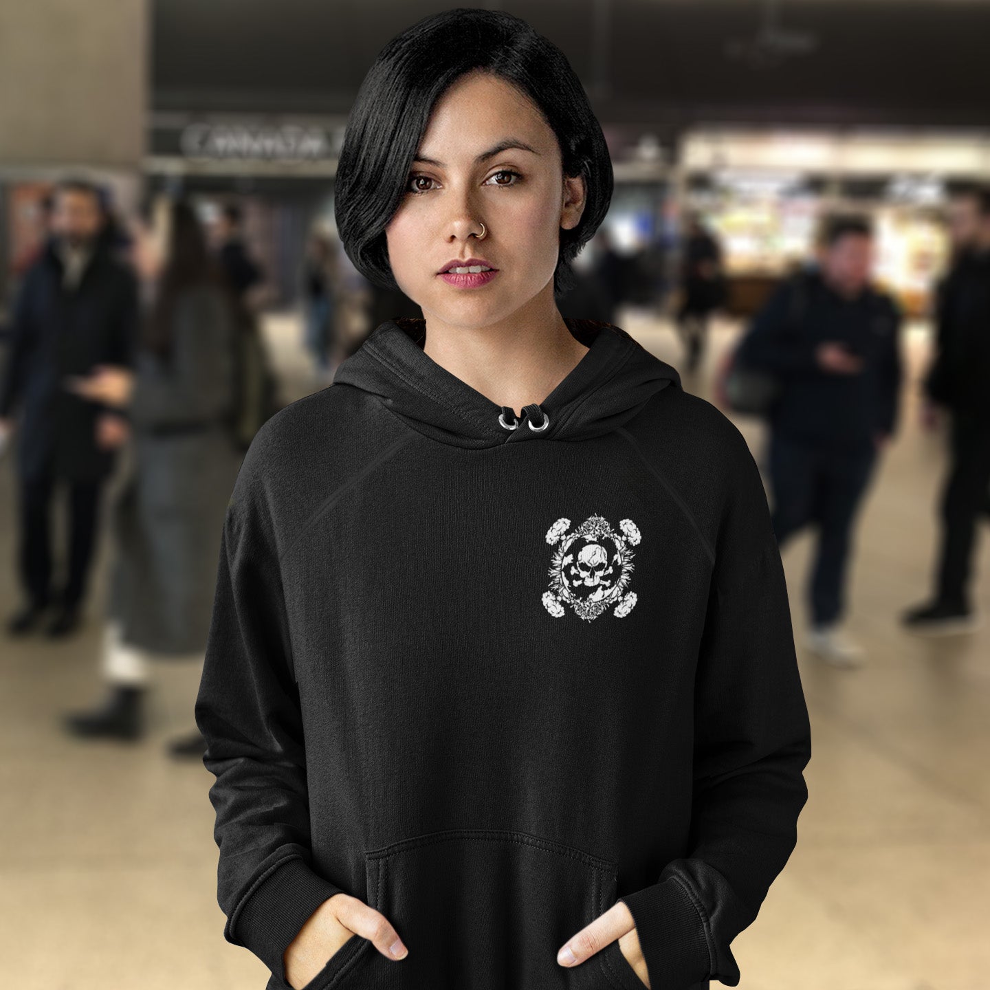 Person wearing a black hoodie with a skull design in a blurred indoor setting. A save the planet hoodie about human impact on nature. An Earth day special. This design highlights the amount of death and destruction we create as a species. An urban art hoodie design for nature lovers. Comfortable and practical. It's extra soft and has a convenient front pouch pocket. Made from organic cotton and recycled polyester, this social issues hoodie is a great eco-friendly choice.