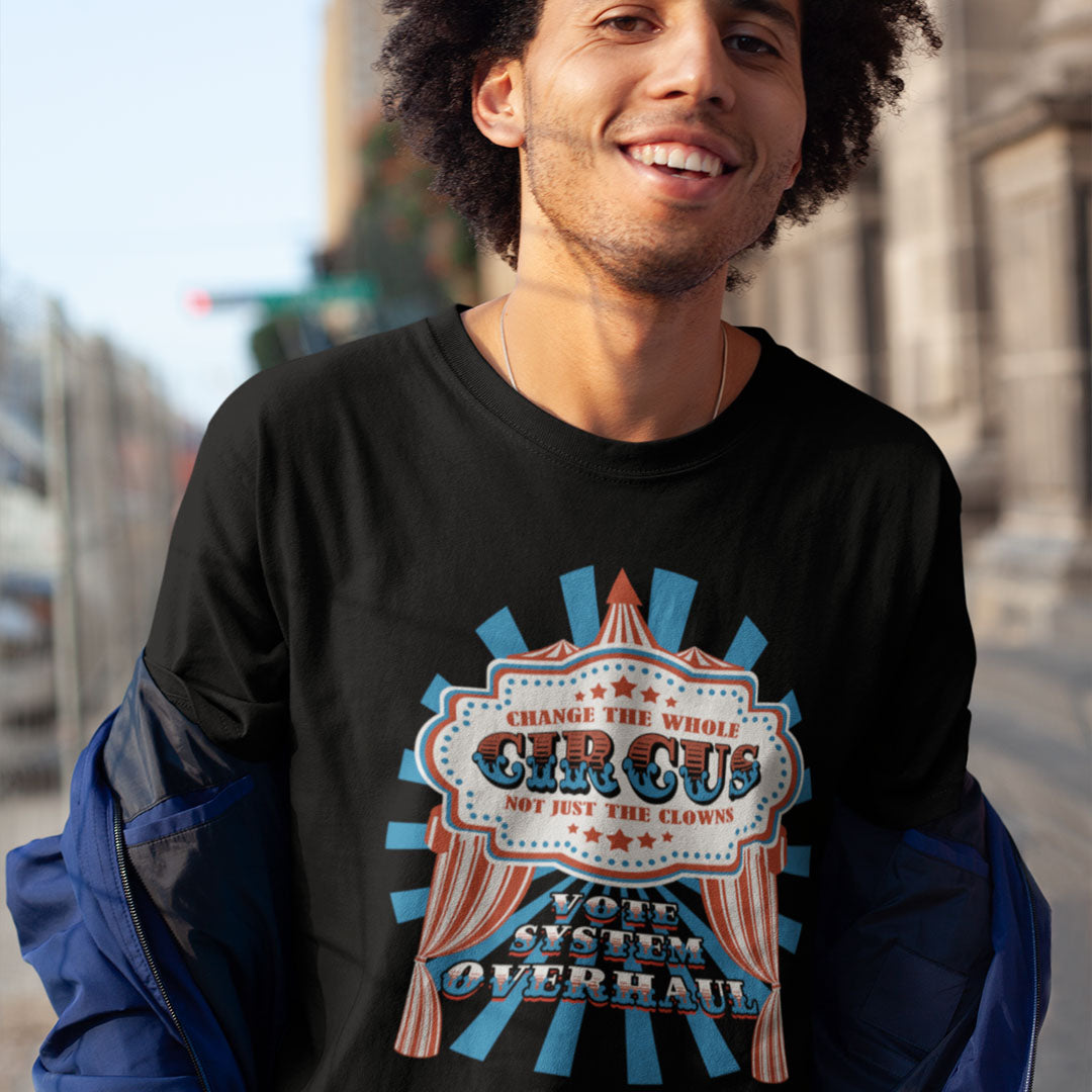 Man wearing a black sweatshirt with a colourful graphic design on a street background. This anti government t shirt points out that you can change the clowns but the circus remains. Does it matter who fronts a corrupt system? The whole circus needs to go. Made from 100% organic ring-spun cotton, this civil rights t shirt is unisex, high-quality, super comfy, and best of all, eco-friendly.
