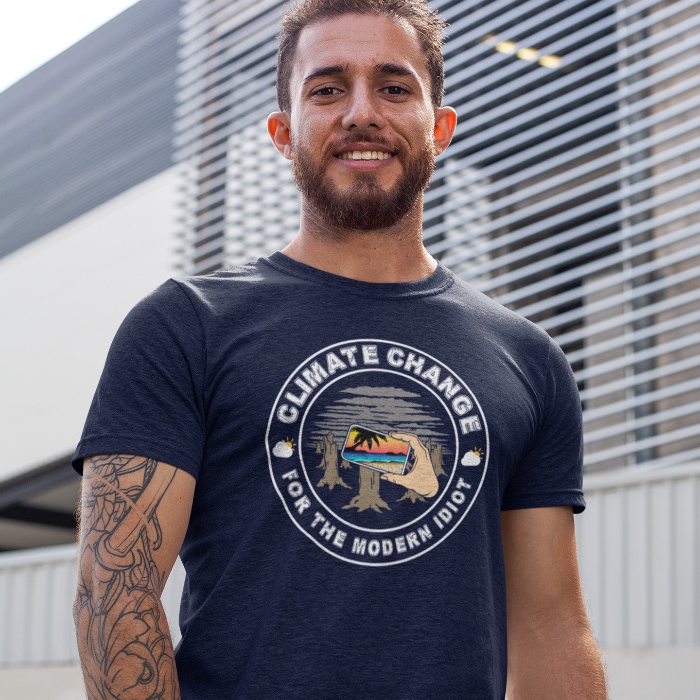 Man wearing a t-shirt with 'Climate Change for the Modern Idiot' design outdoors. A satirical save the planet t-shirt exposing the denial still opposing a very serious issue. In this age of smart technology it's surprising there isn't an app that helps us ignore the environmental crisis. Satire at it's best. Made from 100% organic ring-spun cotton, this save the world t shirt is unisex, high-quality, super comfy, and best of all, eco-friendly.