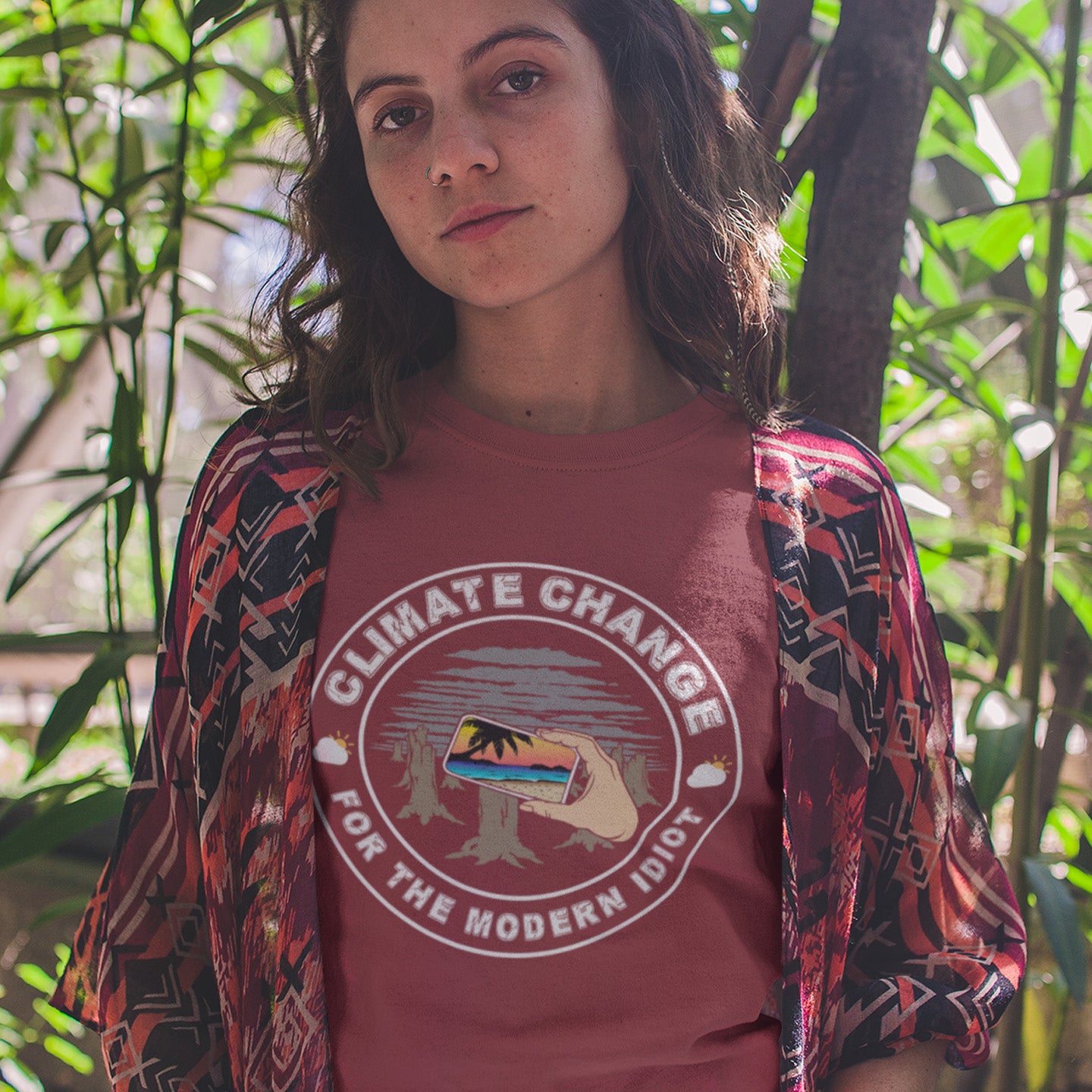 Person wearing a burgundy t-shirt with 'Climate Change for the Modern Idiot' graphic in a natural setting. A satirical save the planet t-shirt exposing the denial still opposing a very serious issue. In this age of smart technology it's surprising there isn't an app that helps us ignore the environmental crisis. Satire at it's best. Made from 100% organic ring-spun cotton, this save the world t shirt is unisex, high-quality, super comfy, and best of all, eco-friendly.