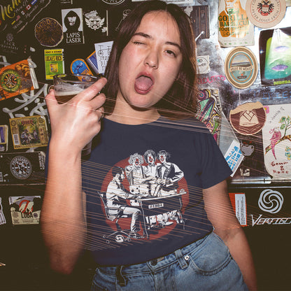 A woman in a bar, holding a drink, with one eye closed and her mouth open, wearing a French navy blue short sleeved crew neck t-shirt with a white and red graphic of three clowns laughing and pointing at an office worker.