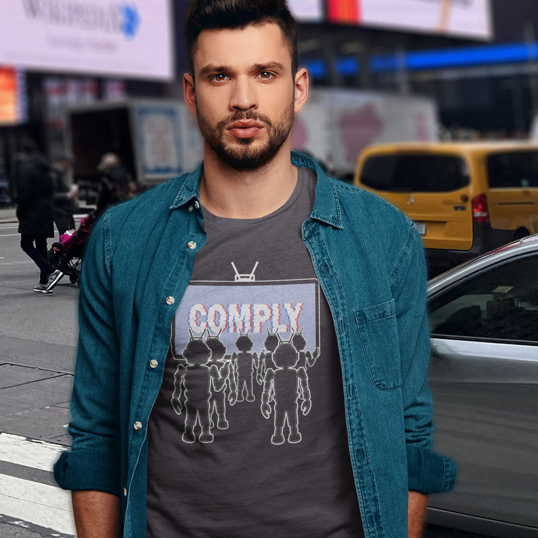 Man wearing a denim jacket over a graphic t-shirt with 'COMPLY' text on a city street. A non conformist t shirt portraying mistrust for the media. This satirical design highlights the television's role in modern day manipulation and mind control. With social media now being blamed for misinformation and gaslighting, the TV is the Godfather of brainwashing. Made from 100% organic ring-spun cotton, this counter culture t shirt is unisex, high quality, super comfy, and best of all, eco-friendly.