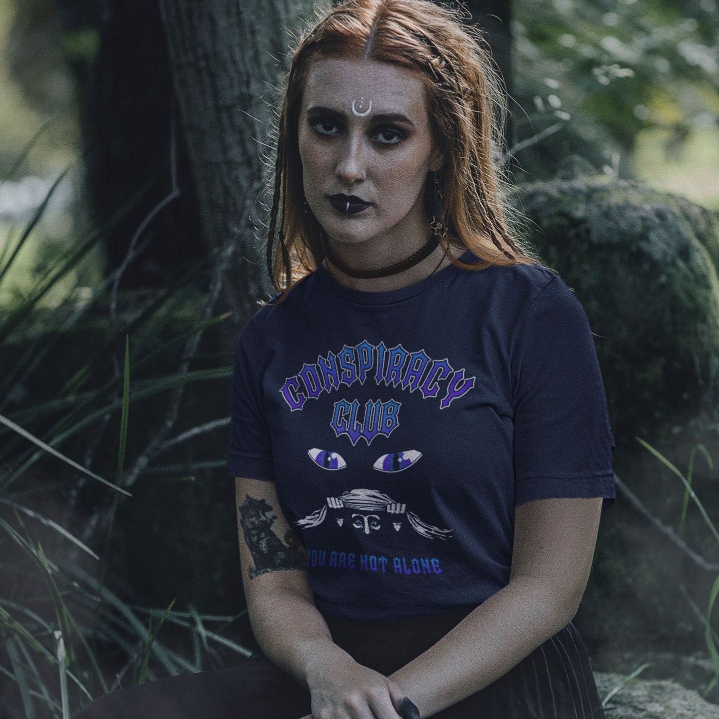 Person wearing a 'Conspiracy Club' t-shirt in a forest setting. A conspiracy theorist t shirt design for all conspiracy lovers who think big brother is watching. join the club, expand your independent thinking, question everything. Think outside the box. Made from 100% organic ring-spun cotton, this funny conspiracy theory t shirt is unisex, high-quality, super comfy, and best of all, eco-friendly.