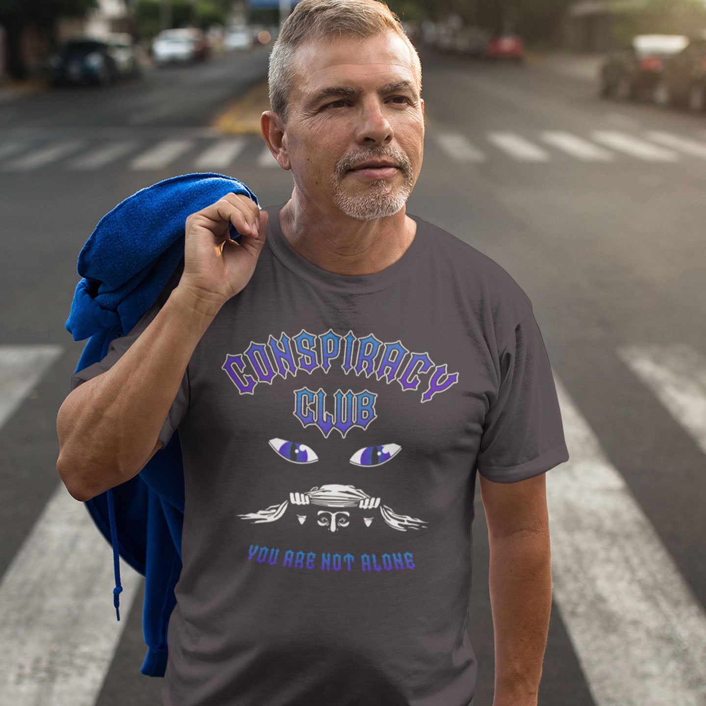 Man wearing a t-shirt with 'Conspiracy Club' design on a street. A conspiracy theorist t shirt design for all conspiracy lovers who think big brother is watching. join the club, expand your independent thinking, question everything. Think outside the box. Made from 100% organic ring-spun cotton, this funny conspiracy theory t shirt is unisex, high-quality, super comfy, and best of all, eco-friendly.