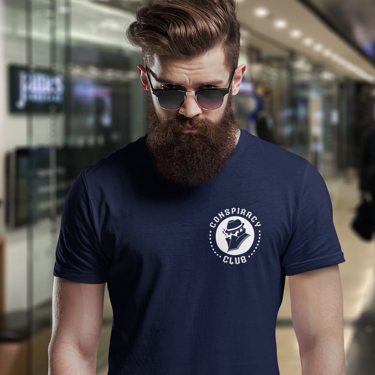 Man wearing a French navy blue t-shirt with 'Conspiracy Club' logo in an indoor setting. A conspiracy theorist t shirt. These days there's a conspiracy theory for every occasion, join the club, expand your alternative imagination. Think outside the box. Underground art on apparel. Made from 100% organic ring-spun cotton, these conspiracy theory t shirts are unisex, high-quality, super comfy, and best of all, eco-friendly.