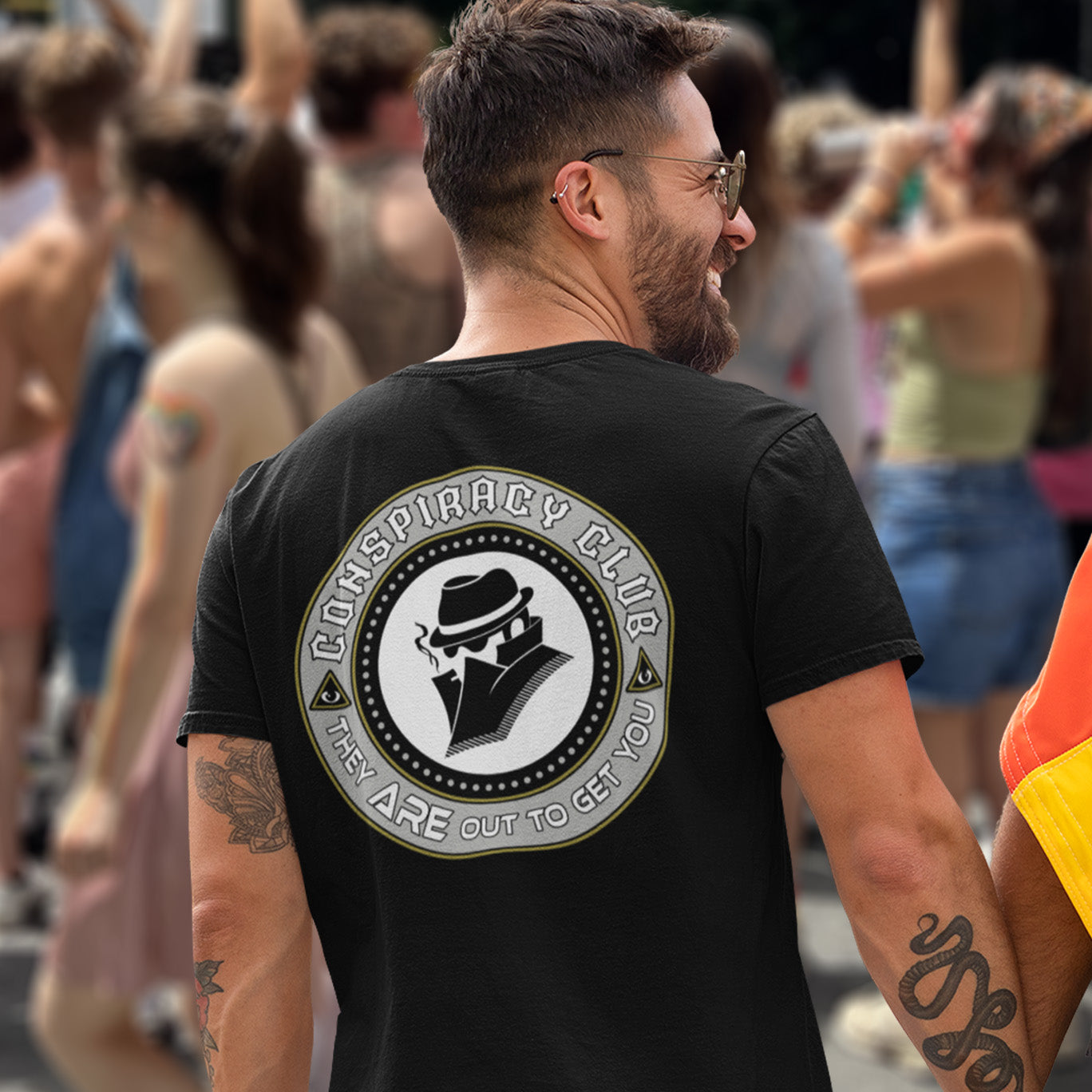 Man wearing a black t-shirt with 'Conspiracy Club' design in a crowd. A conspiracy theorist t shirt. These days there's a conspiracy theory for every occasion, join the club, expand your alternative imagination. Think outside the box. Underground art on apparel. Made from 100% organic ring-spun cotton, these conspiracy theory t shirts are unisex, high-quality, super comfy, and best of all, eco-friendly.