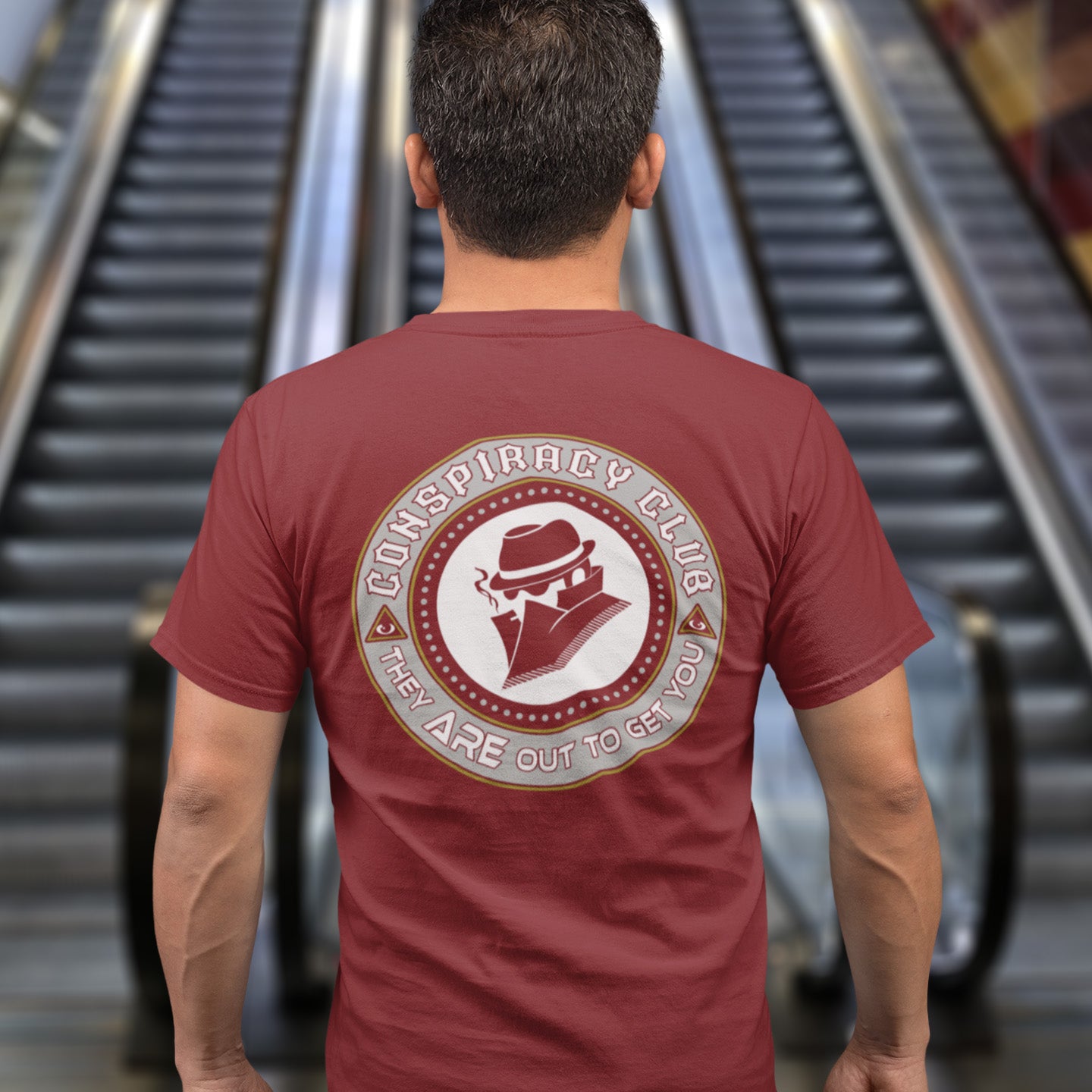 Person wearing a burgundy t-shirt with a conspiracy theory graphic in front of an escalator. A conspiracy theorist t shirt. These days there's a conspiracy theory for every occasion, join the club, expand your alternative imagination. Think outside the box. Underground art on apparel. Made from 100% organic ring-spun cotton, these conspiracy theory t shirts are unisex, high-quality, super comfy, and best of all, eco-friendly.